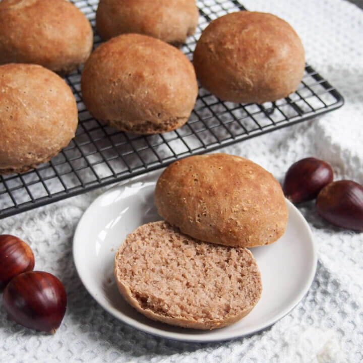 sliced open chestnut bread roll on plate with more rolls behind