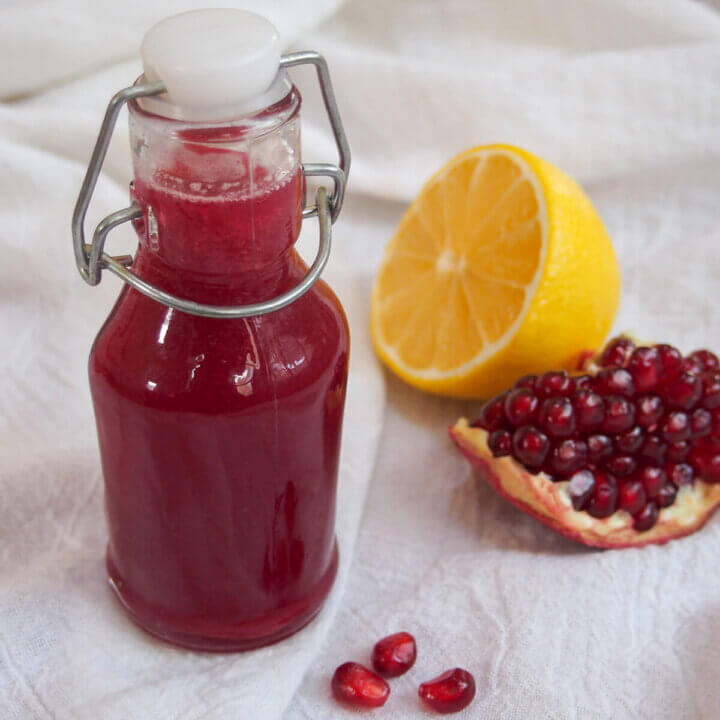 bottle of homemade grenadine with lemon and pomegranate to side