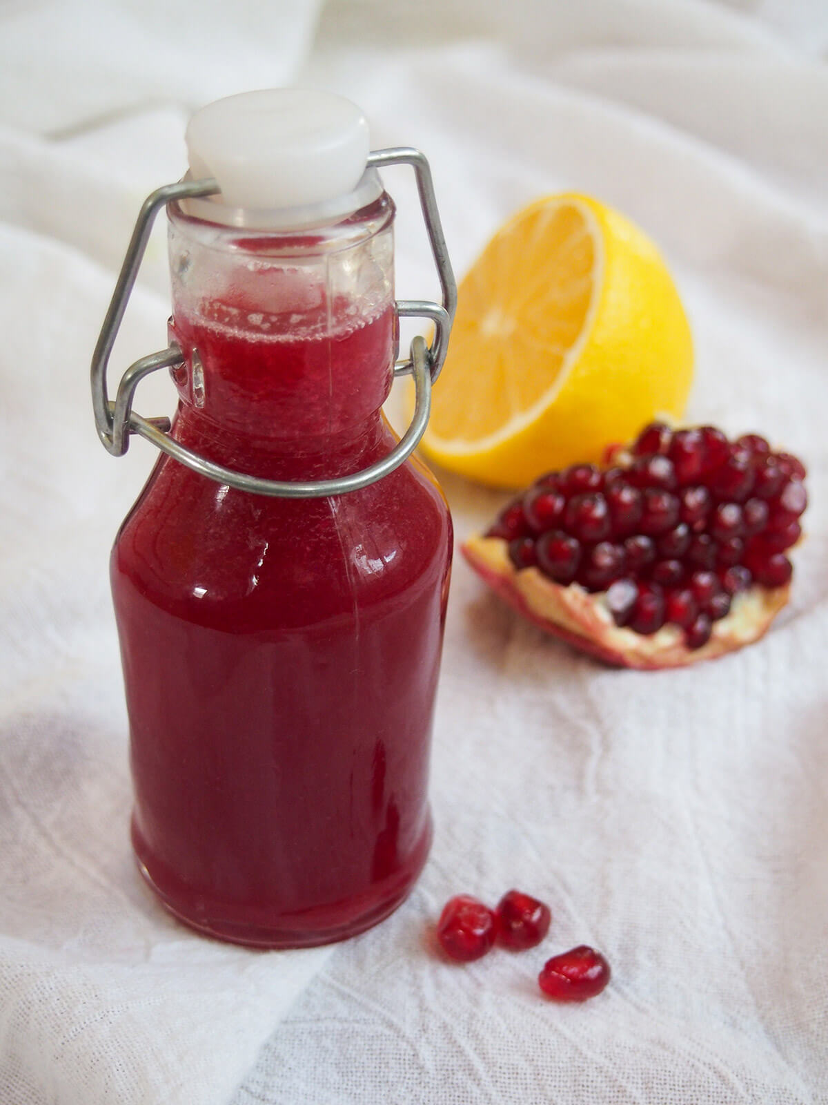 bottle of homemade grenadine with lemon and pomegranate chunk behind