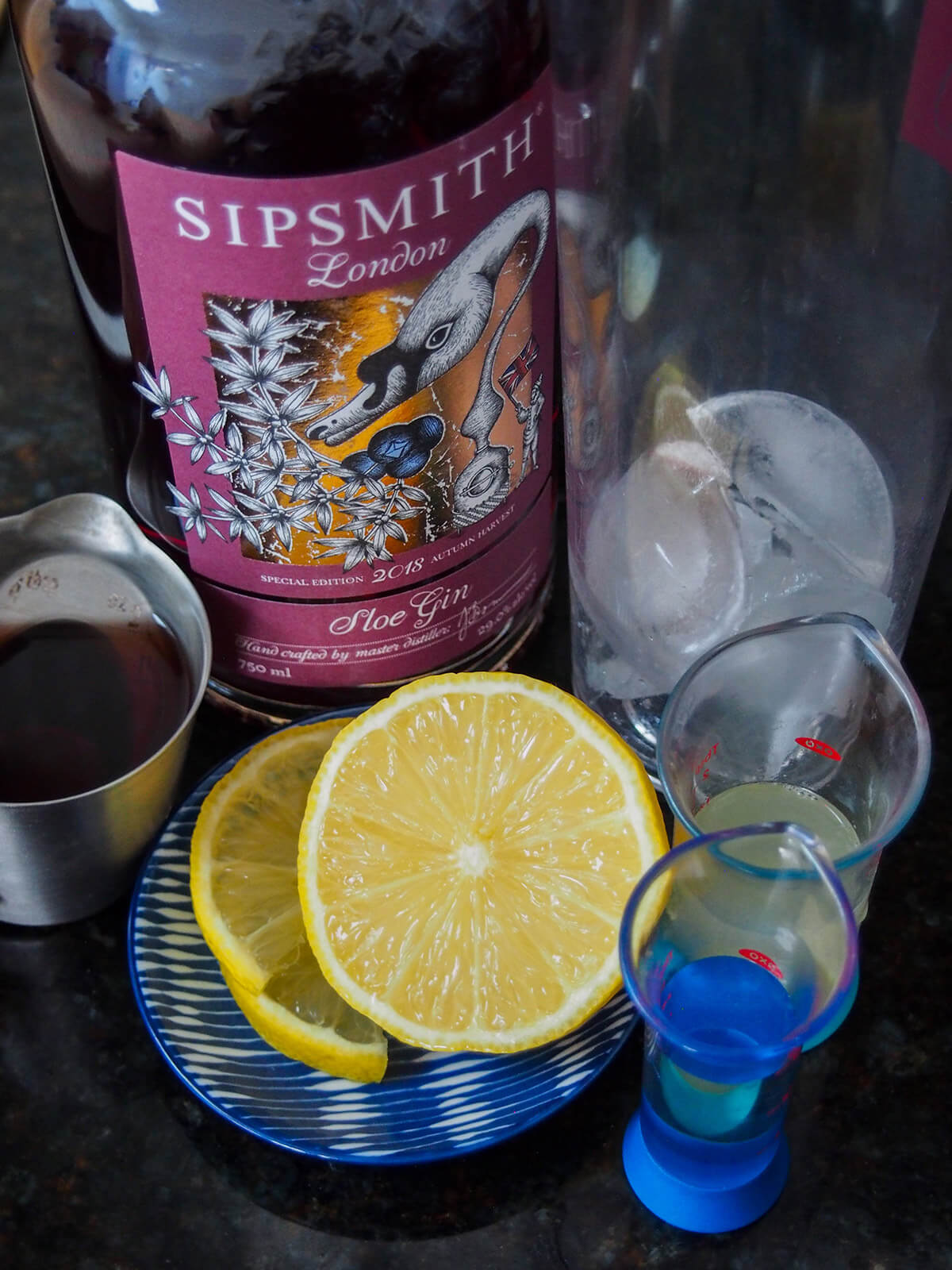 bottle of sloe gin with mixer with ice to side and plate with lemon