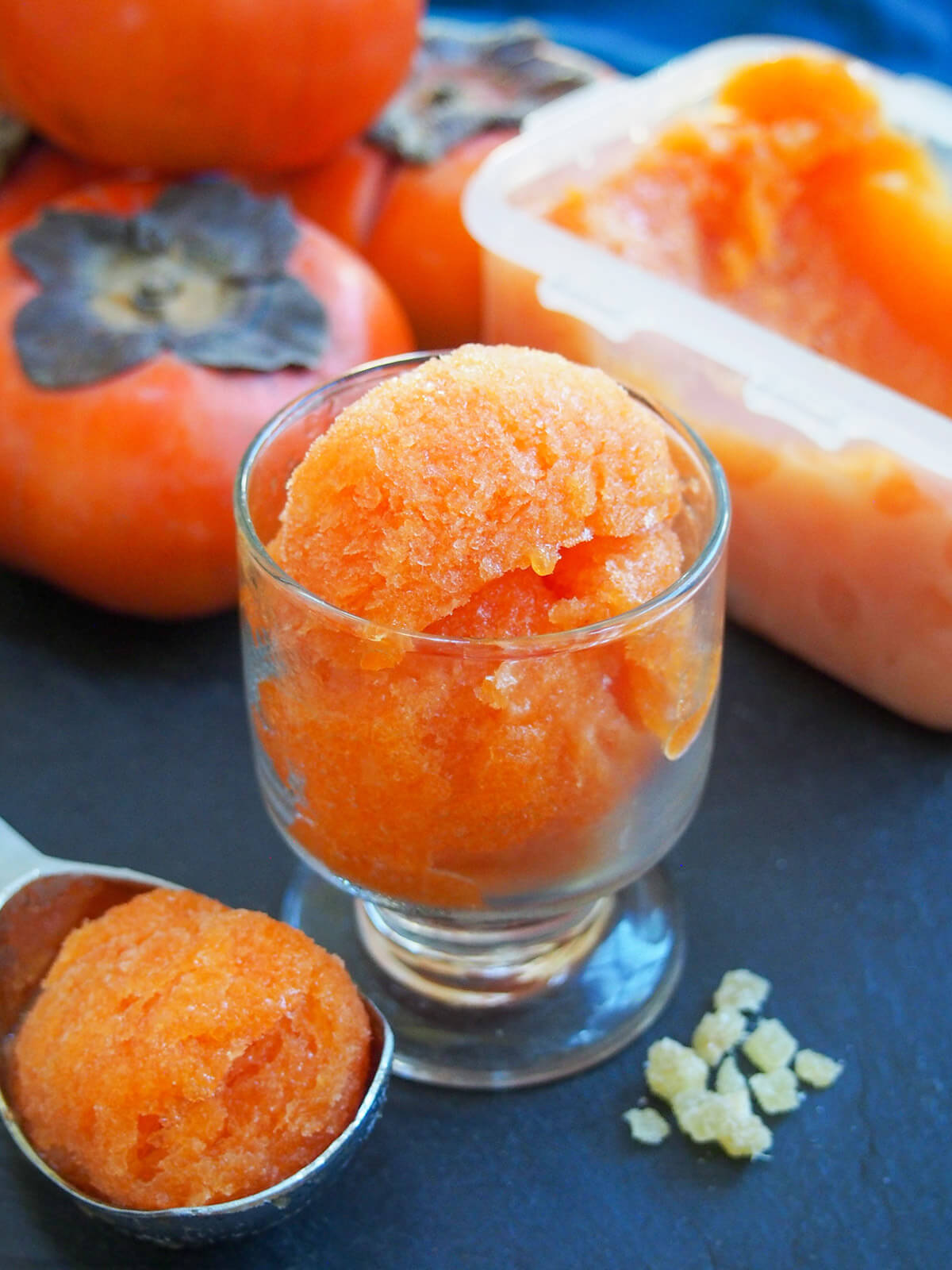 This delicious persimmon ginger sorbet is easy to make and both looks and tastes great. The zingy ginger complimenting the smooth, fragrant persimmon. glass of persimmon ginger sorbet with container and fruit behind