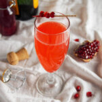 glass of pomegranate French 75 with piece of pomegranate to side