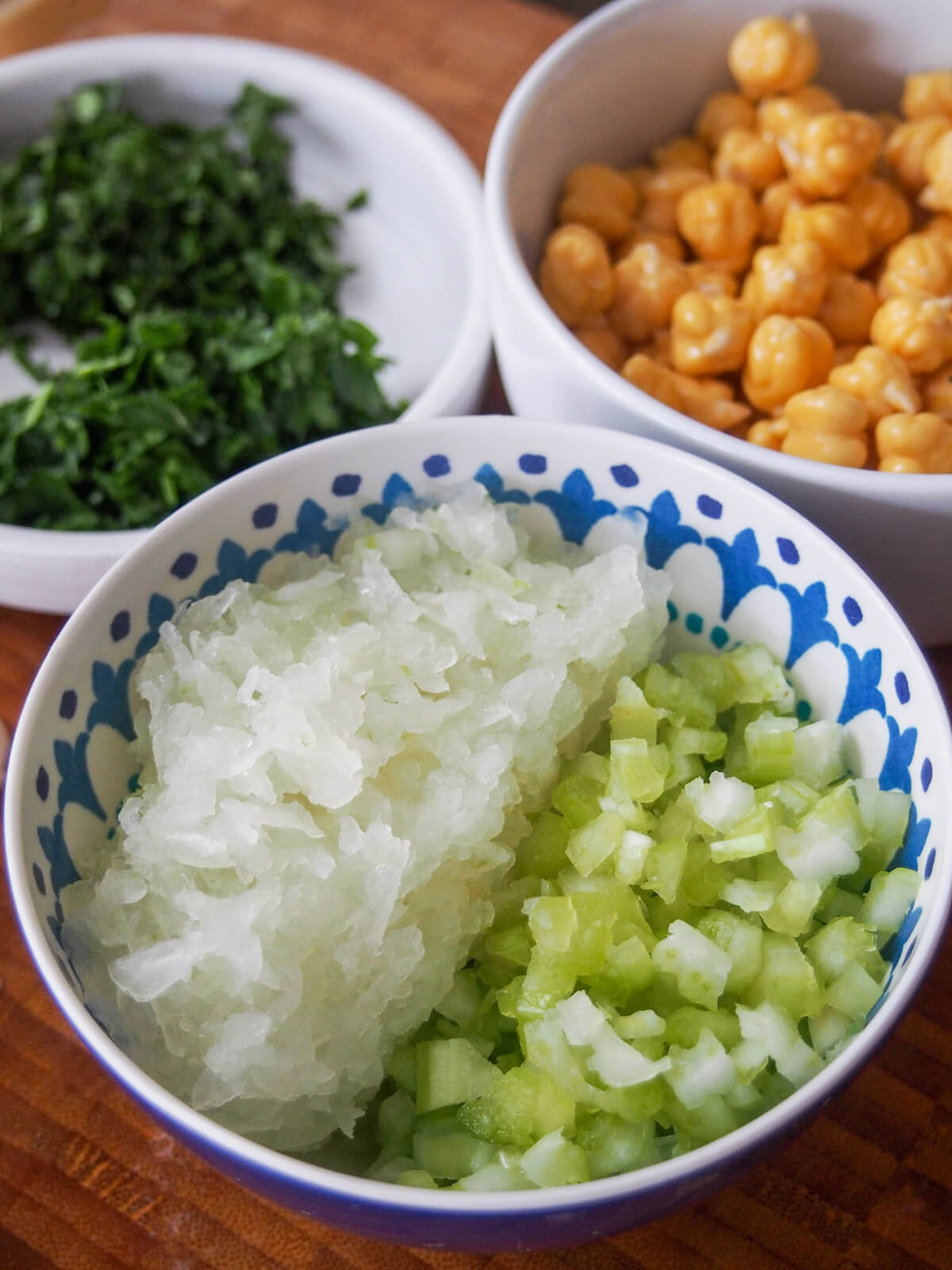 bowl with finely chopped onion and celery with herbs and chickpeas behind