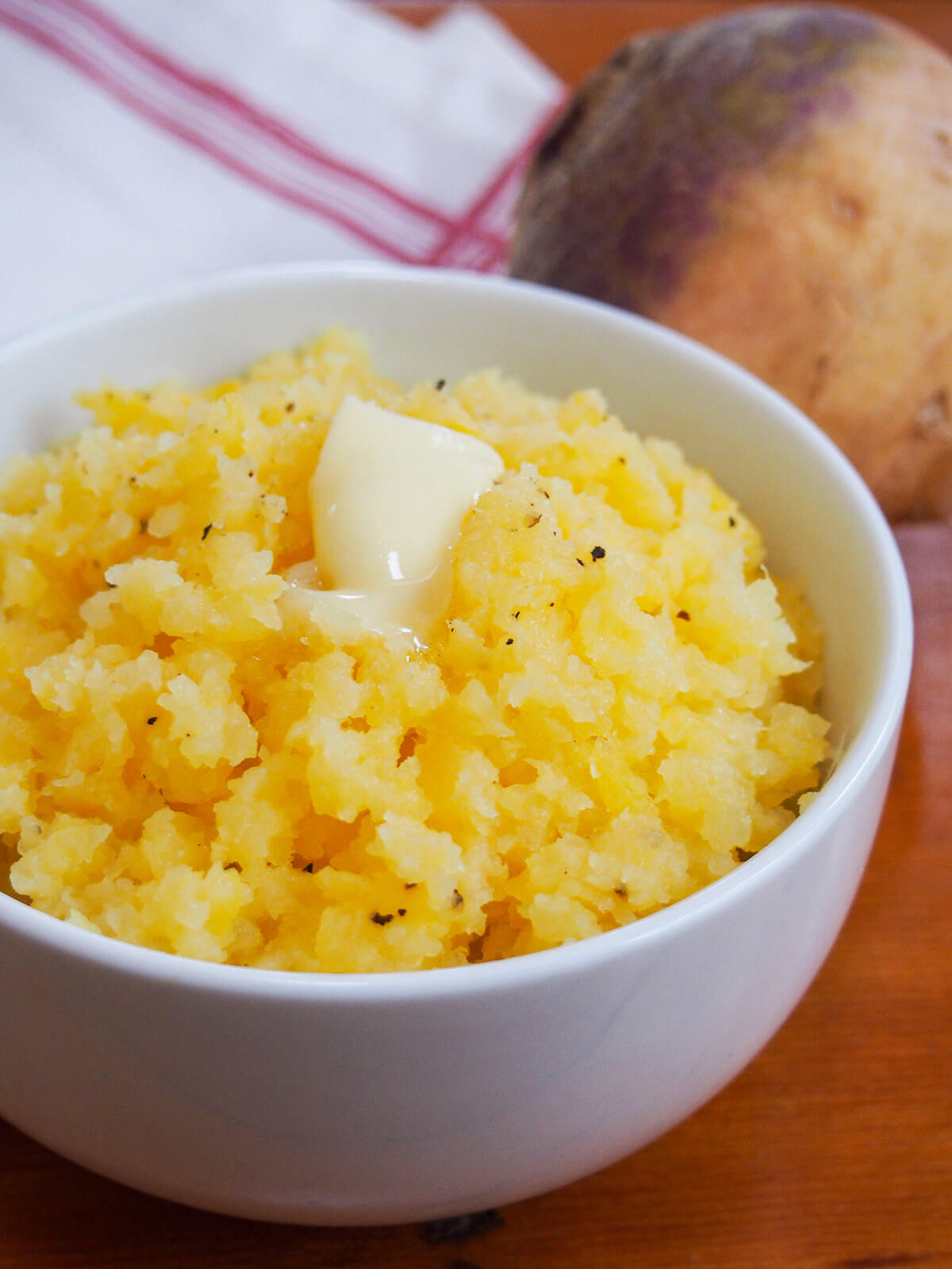 Mashed rutabaga, or swede mash, is an easy side dish and tasty alternative to mashed potato or other root vegetables. It pairs perfectly with a range of mains like roast meats and sausages with a mild and gently sweet flavor. close up of bowl of mashed rutabaga with butter on top