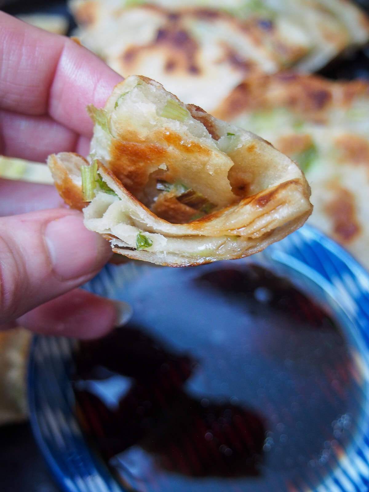 holding a piece of scallion pancake in hand over dipping suce holding a piece of scallion pancake over dipping sauce