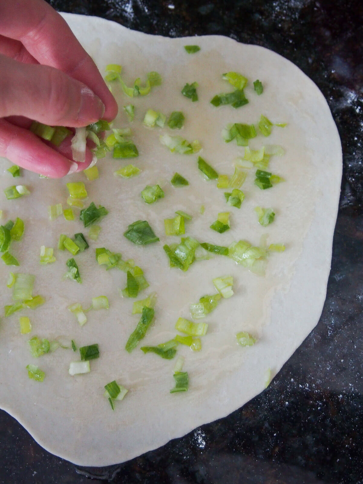 adding scallions on top of scallion pancake dough adding scallions over rolled out dough