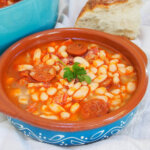 bowl of fabada asturiana with chunk of bread and pot behind