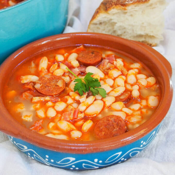 bowl of fabada asturiana with chunk of bread and pot behind