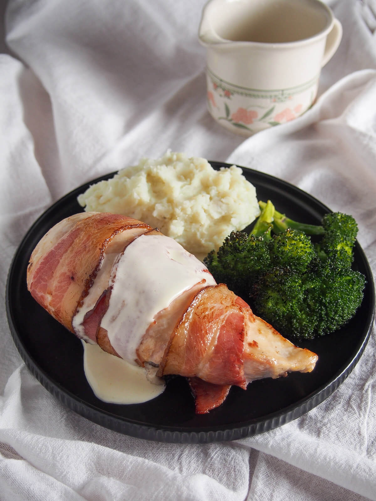 chicken breast wrapped with bacon and drizzled with sauce with sides behind