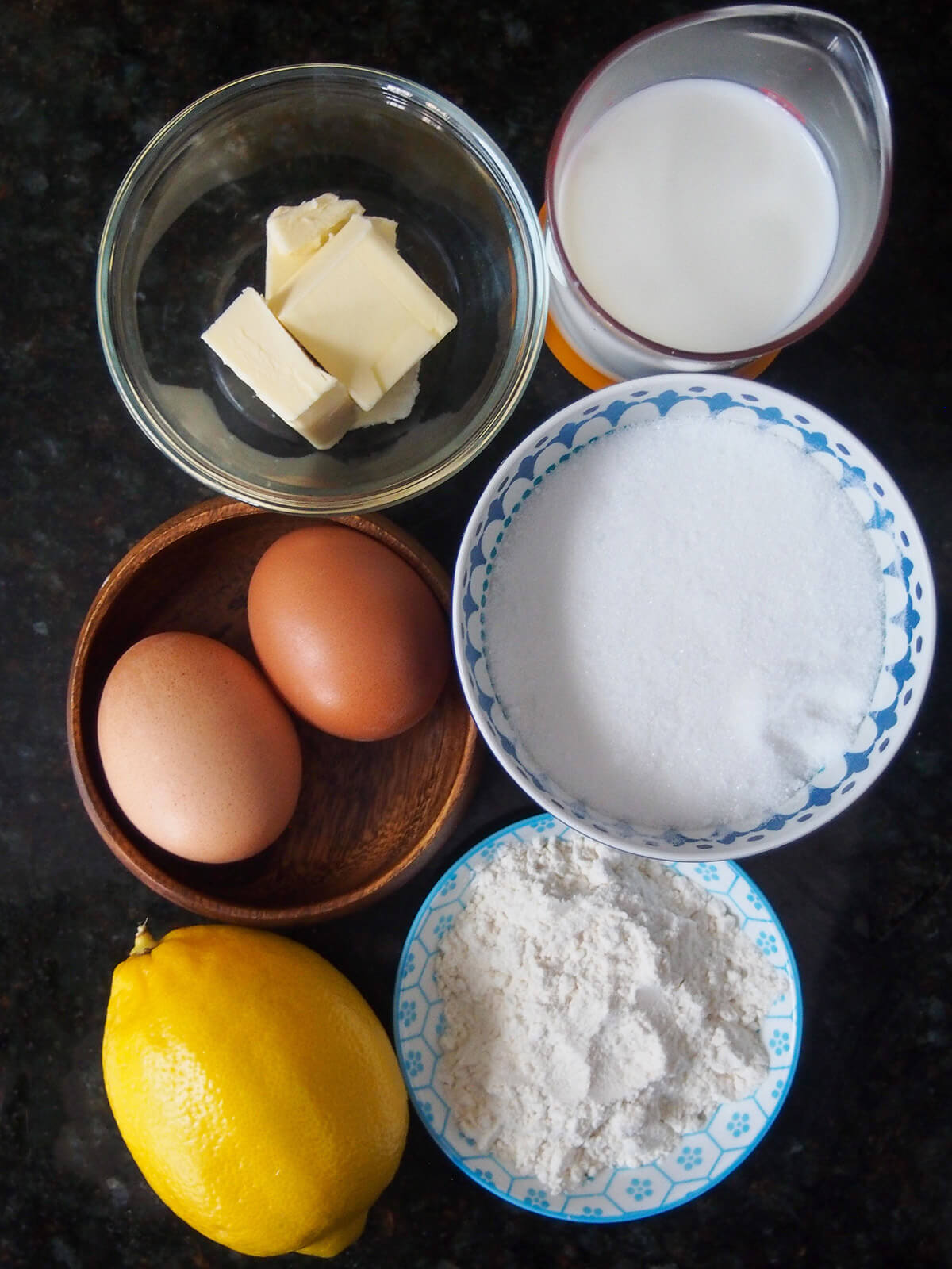 bowl with sugar, flour, butter, milk and eggs with lemon to side