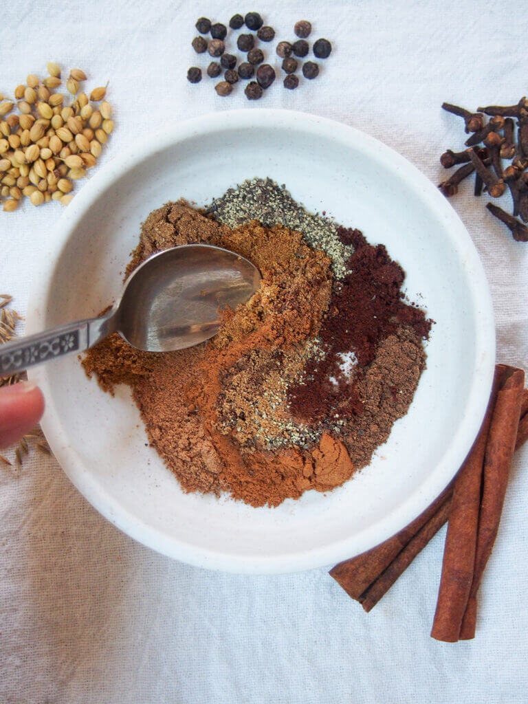 mixing Lebanese seven spice in small dish with whole spices to side