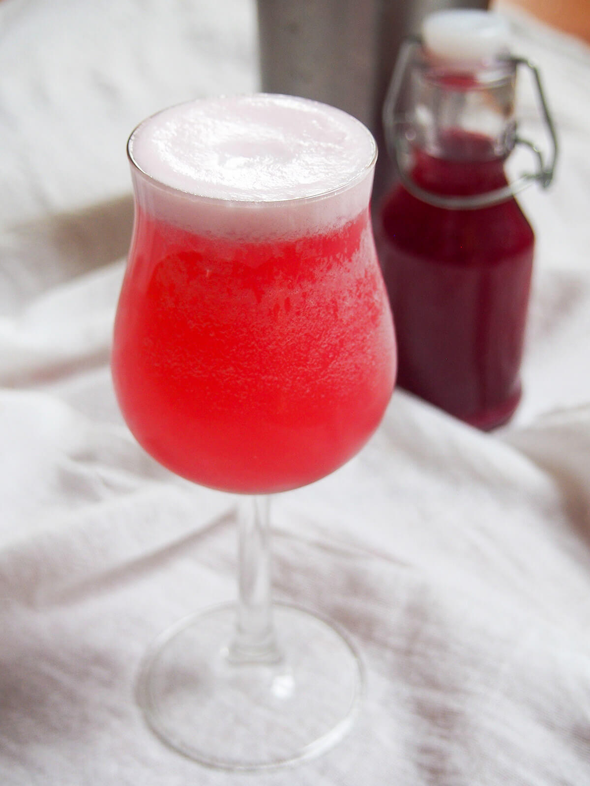 closse view of glass of pink gin fizz with bottle of grenadine behind