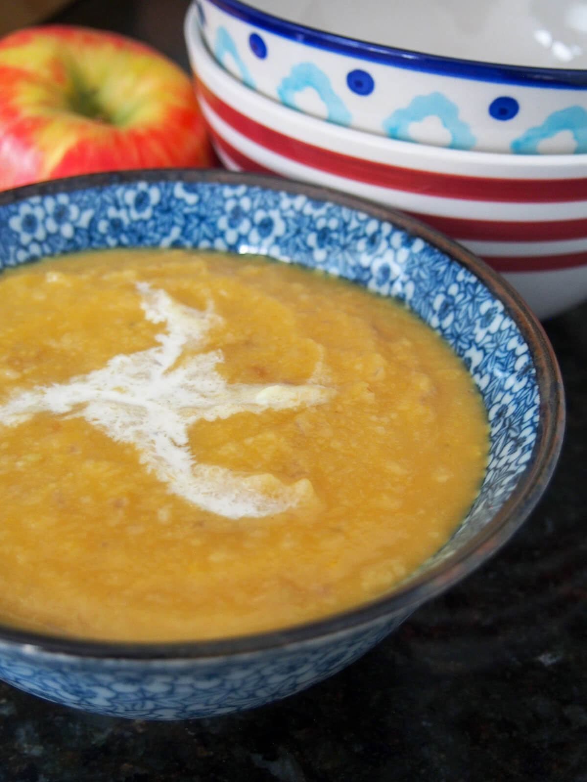 bowl of roasted apple and acorn squash soup from side with bowls stacked behind