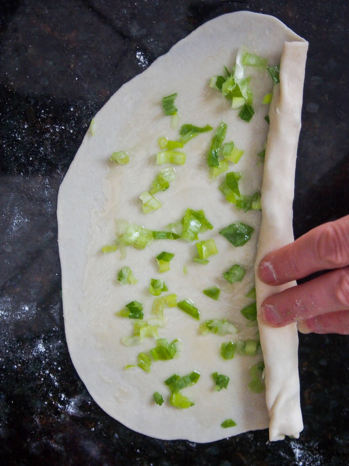 rolling up scallion pancake with pieces of scallion inside rolling up pancake with scallions inside