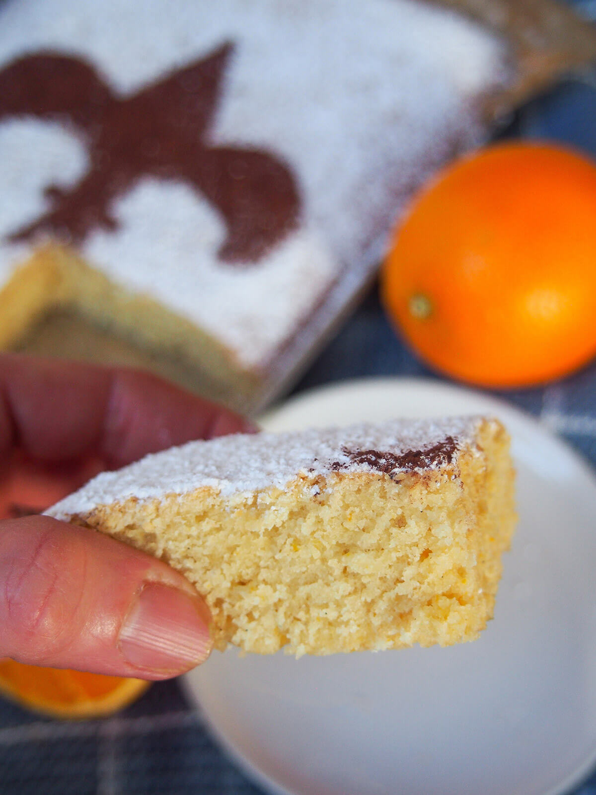 slice of cake held in hand with rest and an orange behind