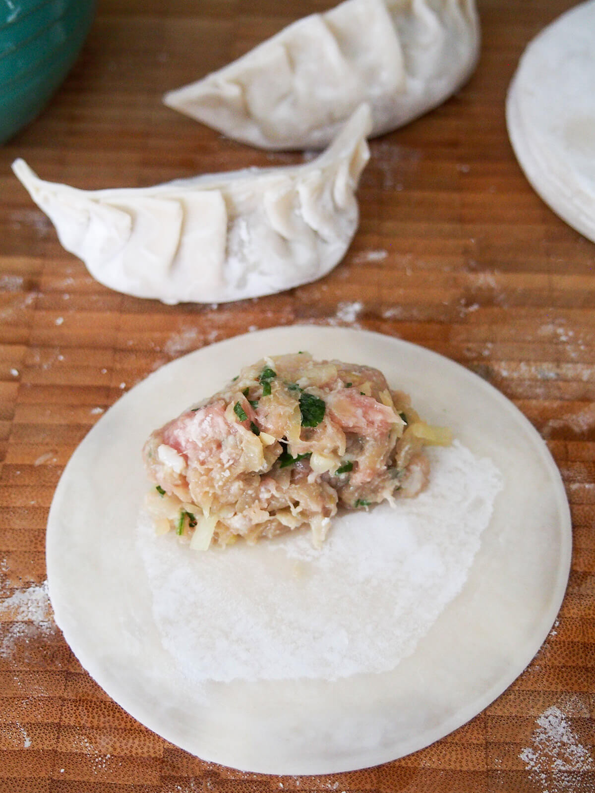 filling Chinese pork and cabbage dumplings adding filling on top of dumpling wrapper with folded dumpling behind