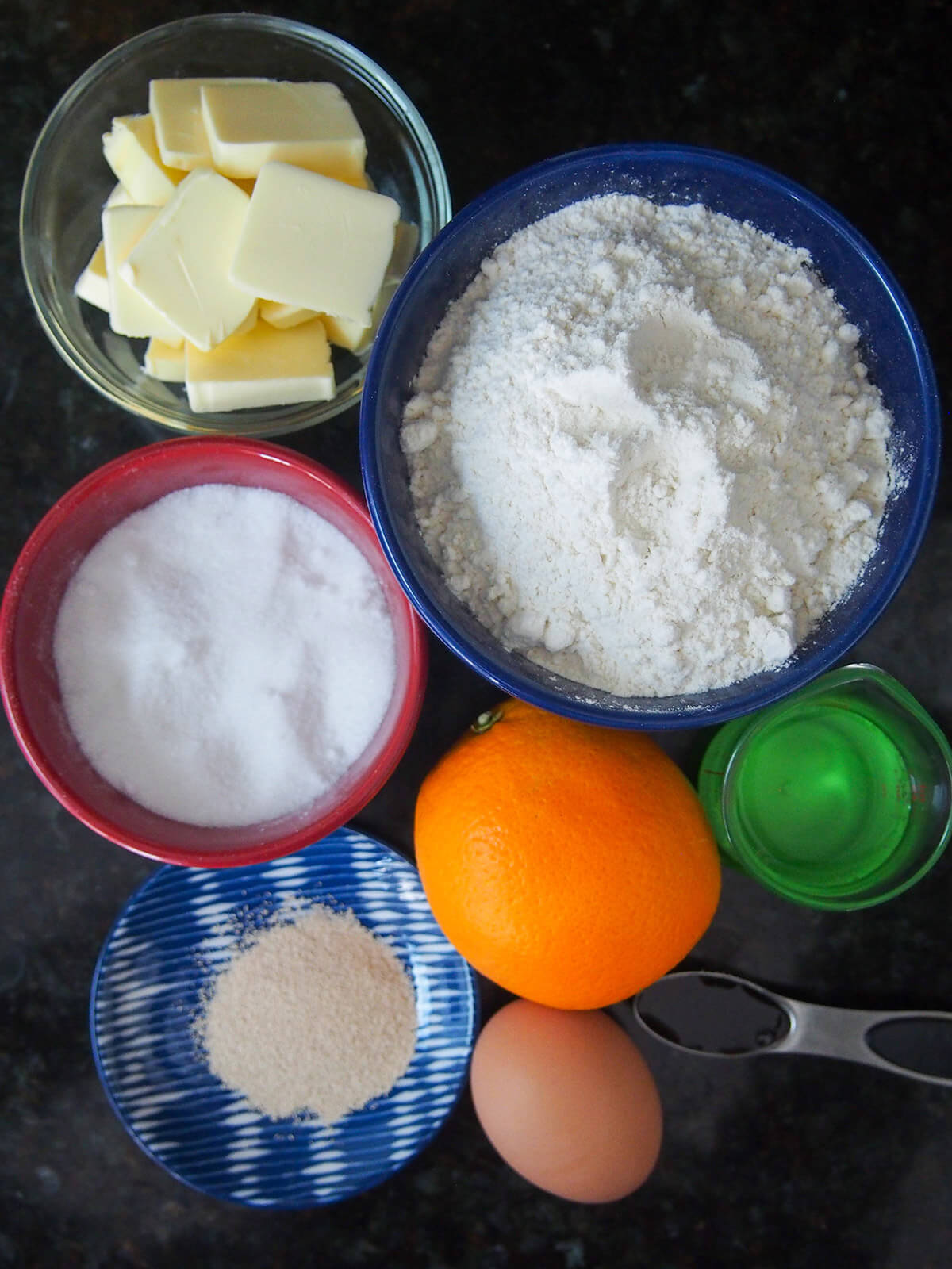 bowls with flour, butter, sugar, yeast, water and egg and orange beside them