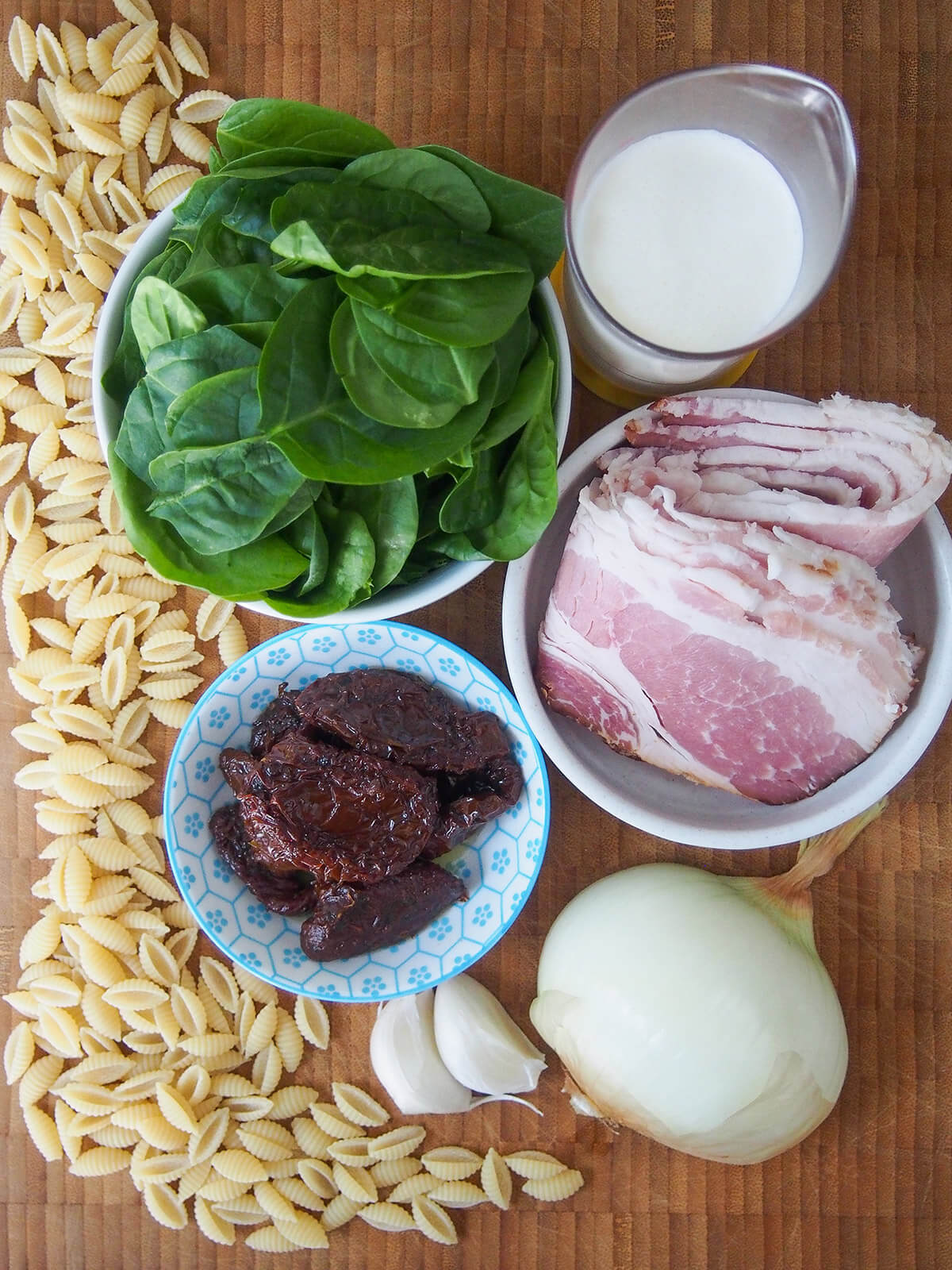 bowls with spinach, bacon, sun dried tomatoes, cream with onion, garlic and pasta to side