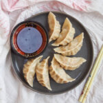 Pork and cabbage dumplings on plate with dipping sauce on side of plate