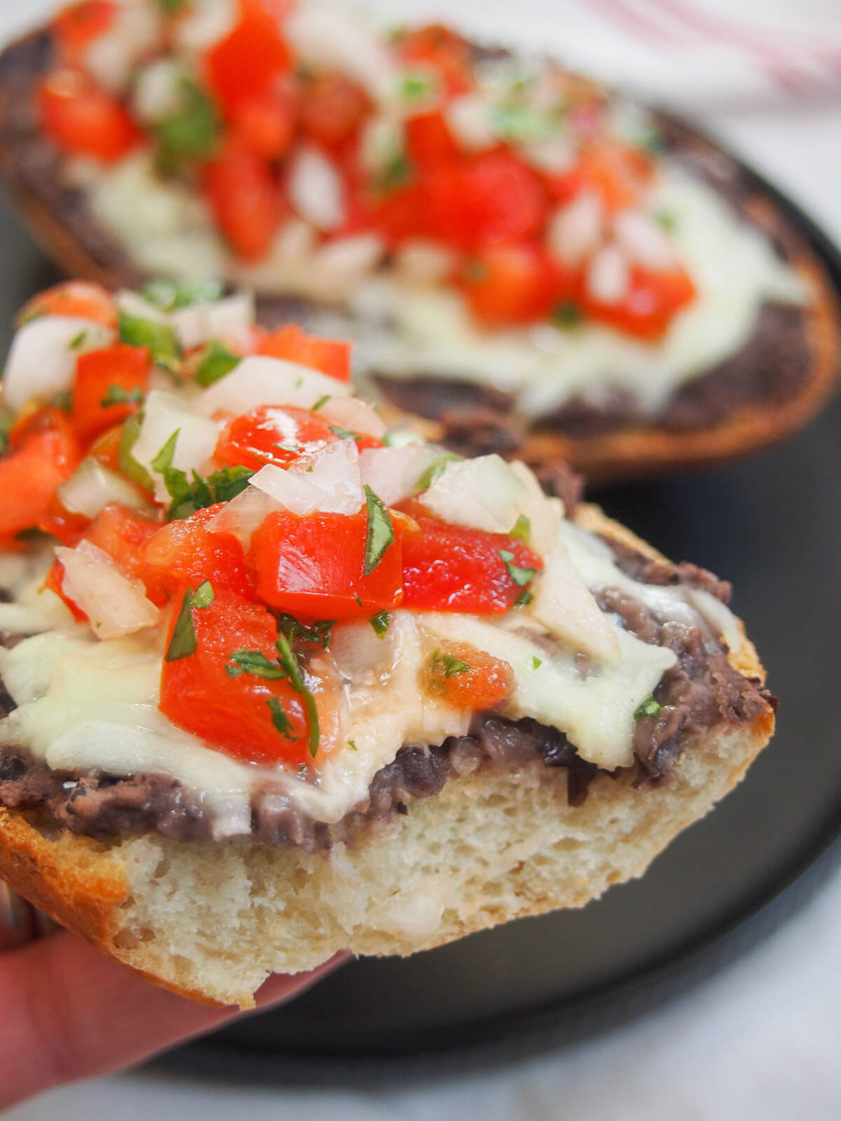 piece of molletes bitten into held in hand in front of plate with more