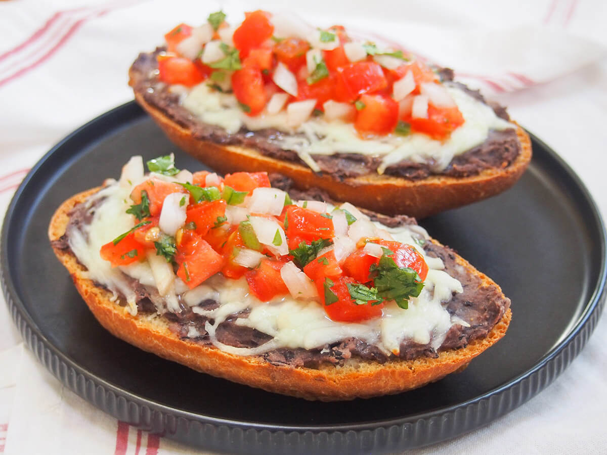black plate with two pieces of Mexican molletes on top