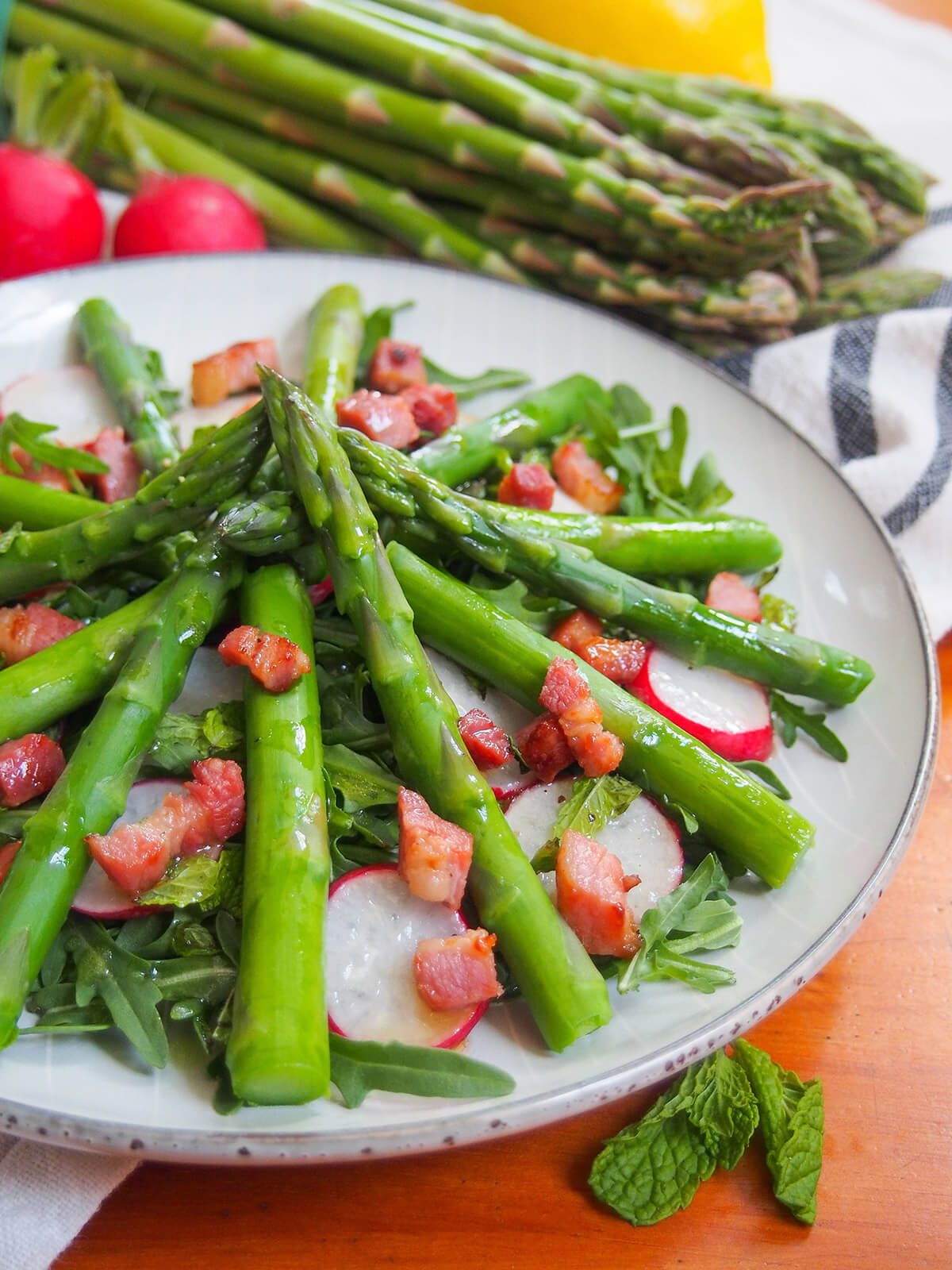 part view of plate of asparagus salad with lemon vinaigrette with bunch of asparagus behind plate