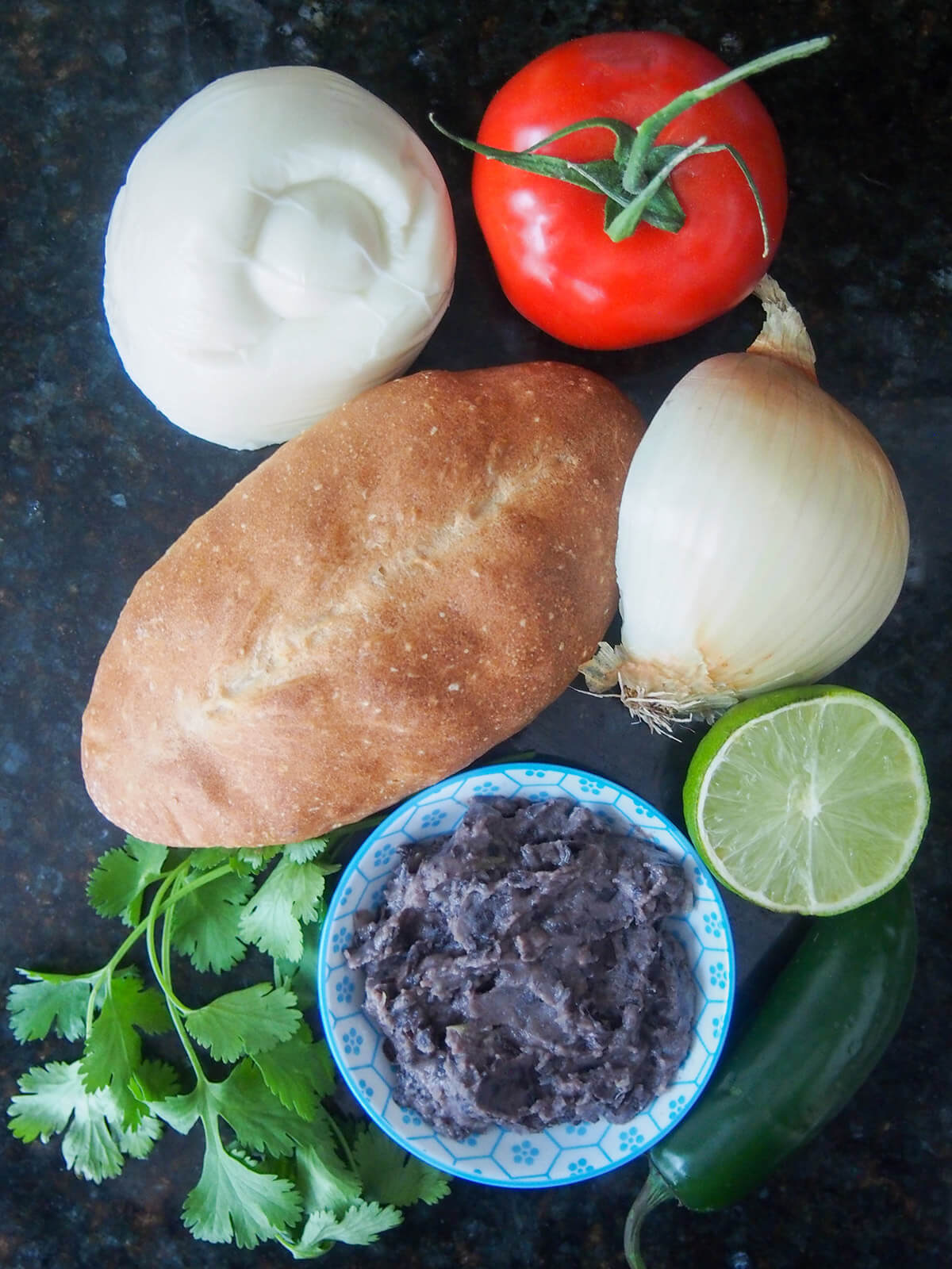 cheese, tomato, onion, lime, chili, bread roll and plate with refried beans