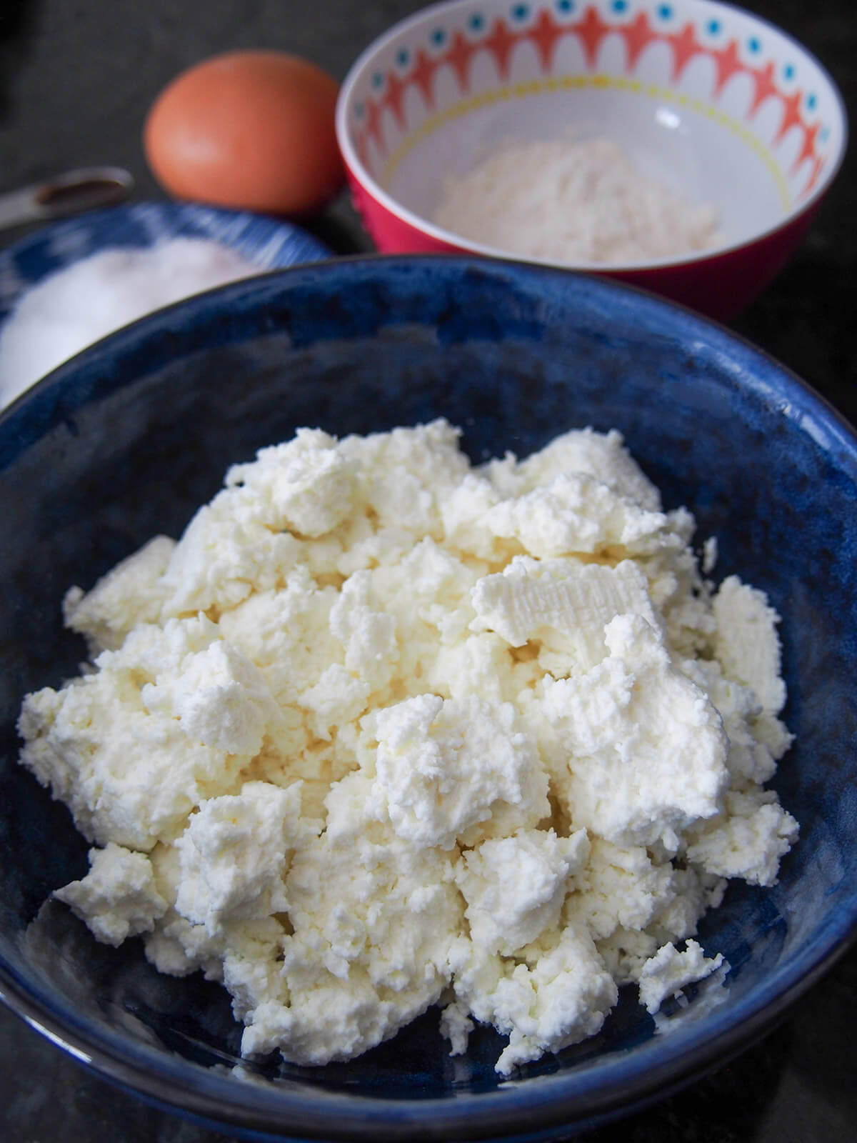 bowl of tvorog curd cheese with bowls of flour, sugar and egg behind