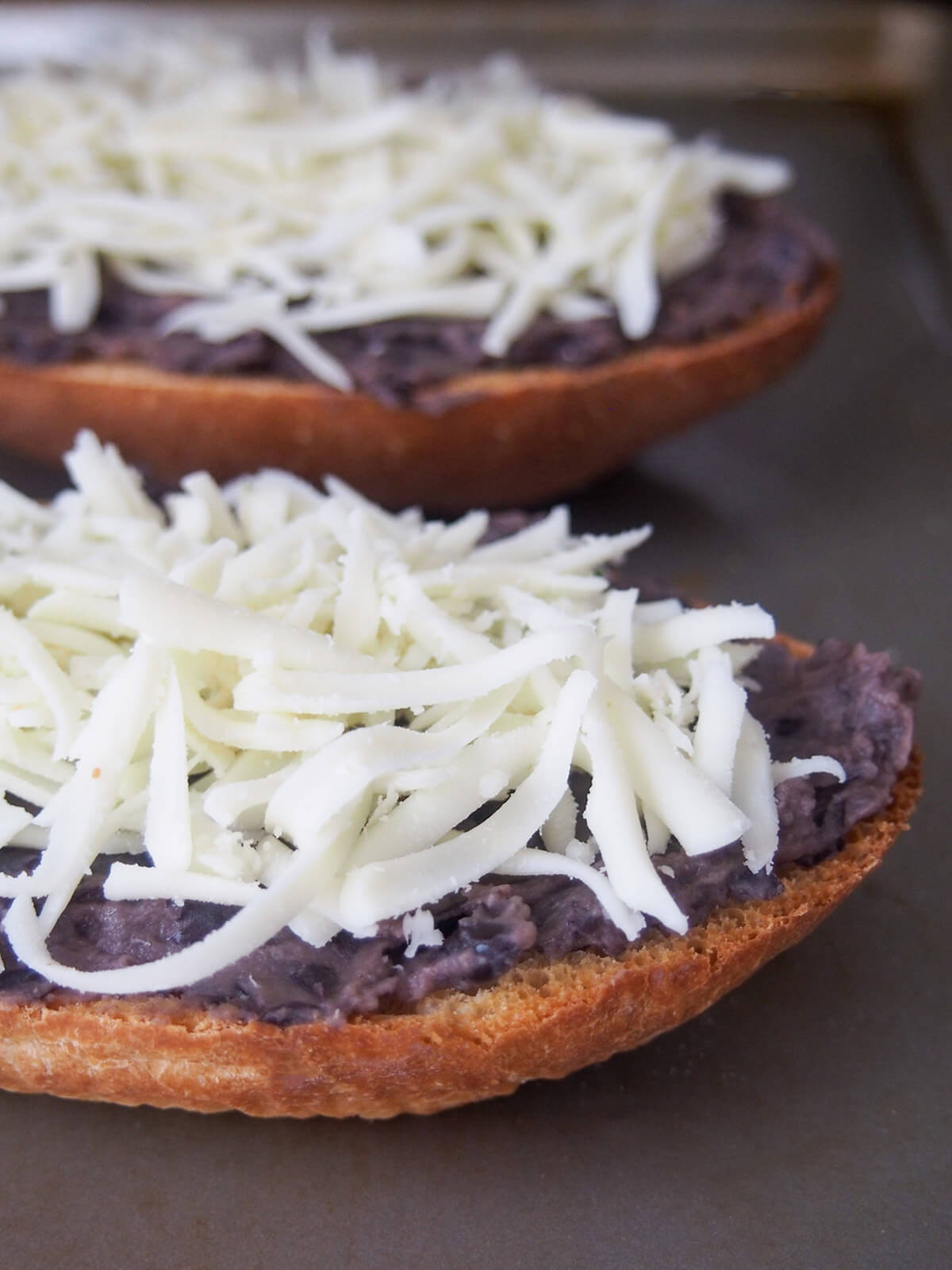 grated cheese on top of refried beans on bread