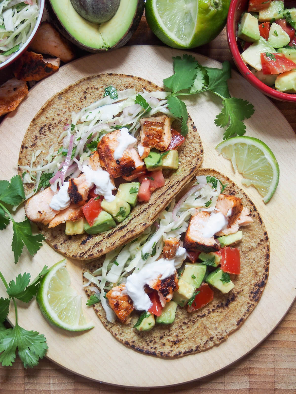 overhead view of two salmon tacos on board with slices of lime and cilantro stems to side