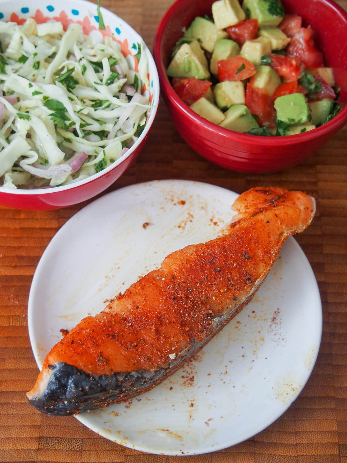 piece of salmon with seasoning on it before cooking with bowls with slaw and chunky salsa behind