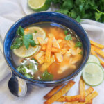 bowl of Mexican lime soup with spoon to side of bowl and slices of lime and tortilla strips on other