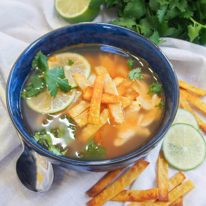 bowl of Mexican lime soup with spoon to side of bowl and slices of lime and tortilla strips on other