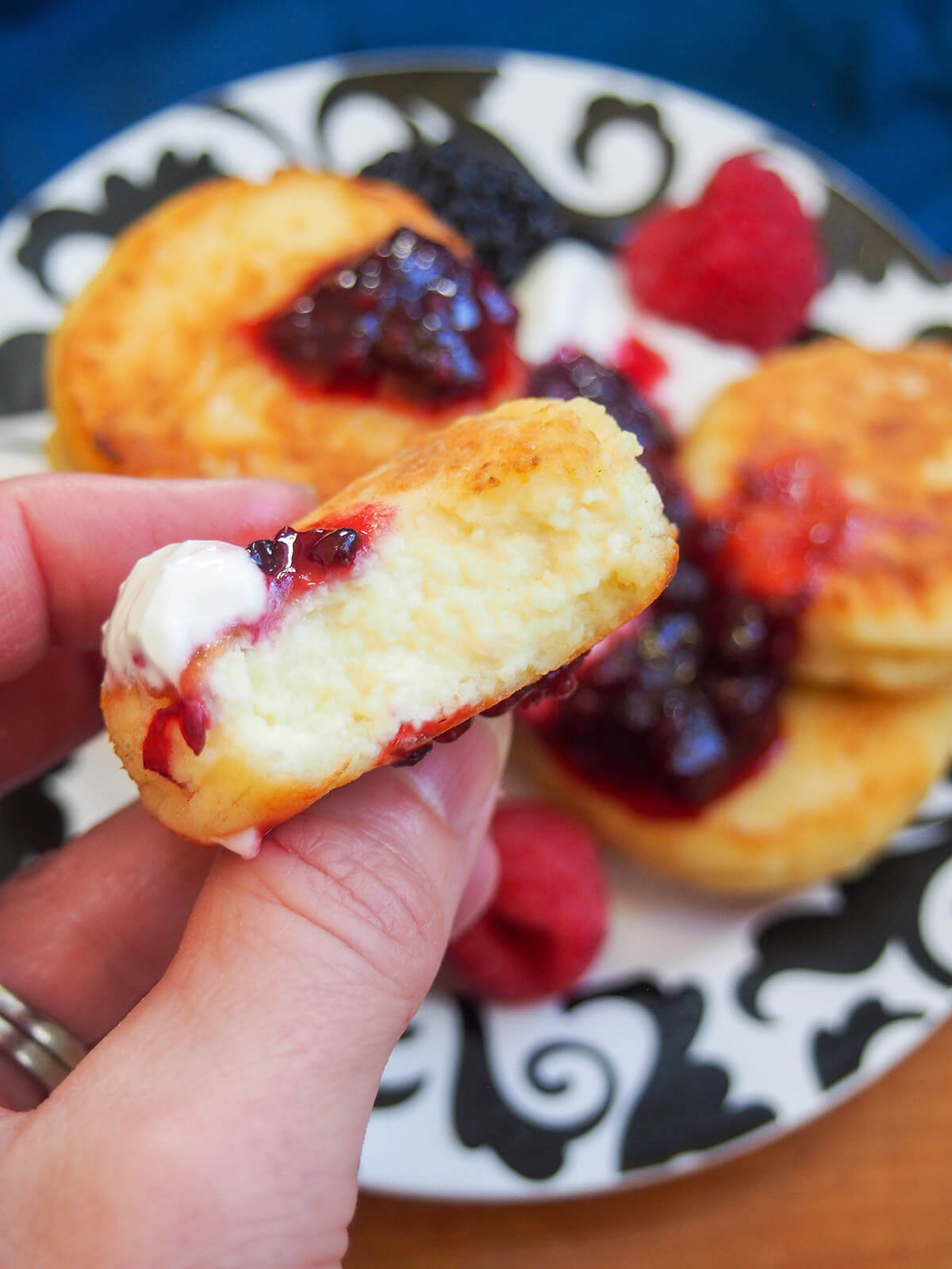 holding a cheese pancake with a bite out of it in hand over plate with more