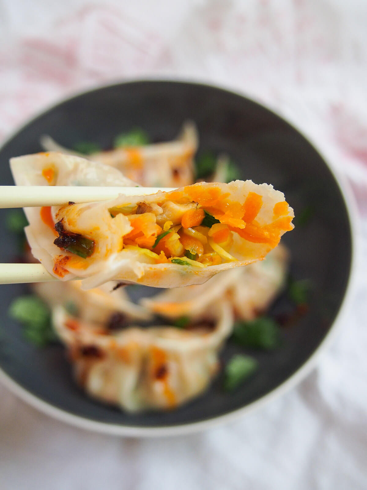 holding a bitten vegetable dumpling over bowl with chopsticks
