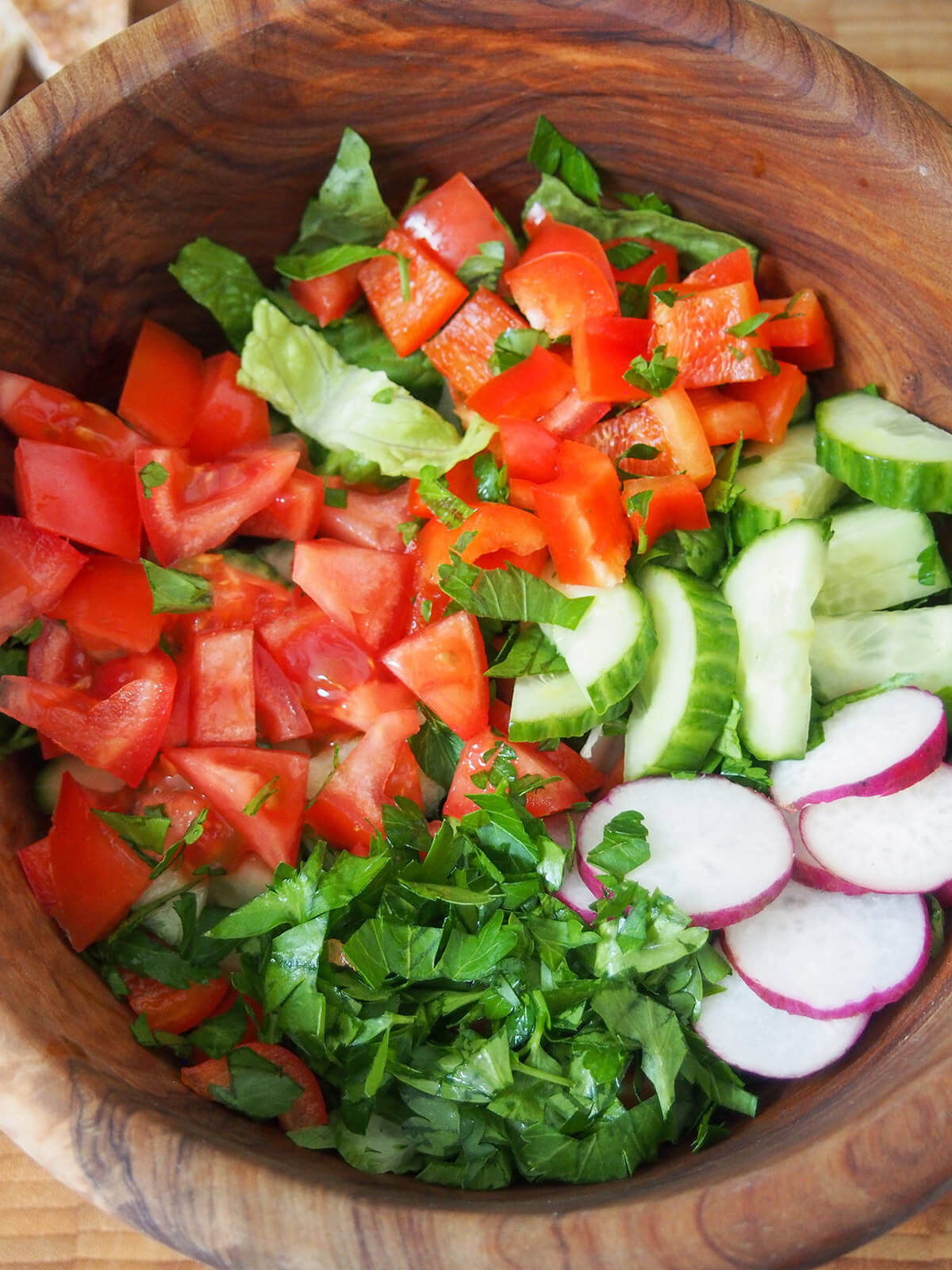 bowl with chopped tomatoes, pepper, cucumber, radish and parsley on top