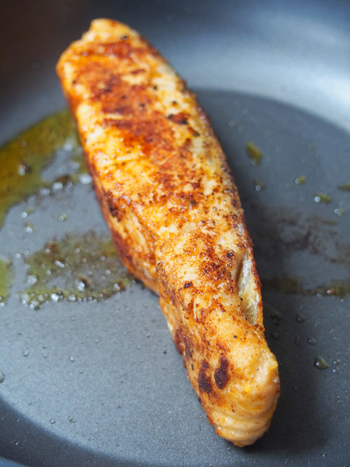 cooking salmon with seasoning on it in skillet
