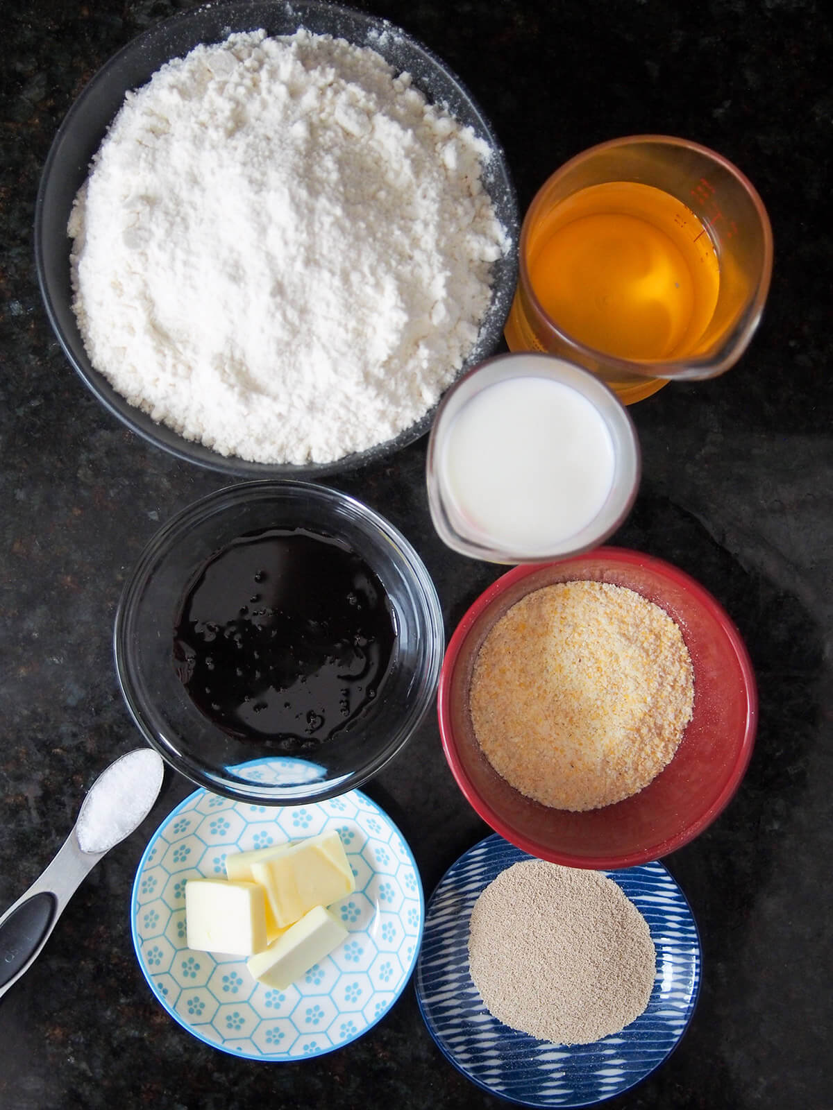 bowls with flour, cornmeal, molasses, yeast, butter and measures with milk and water