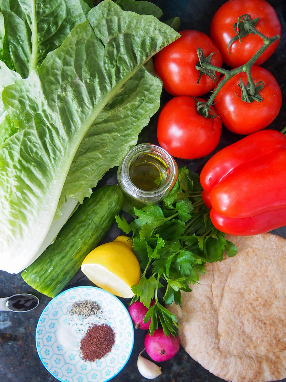 bunch of lettuce, tomatoes, pepper, pita, cucmber, parsley and radishes with part lemon and some olive oil