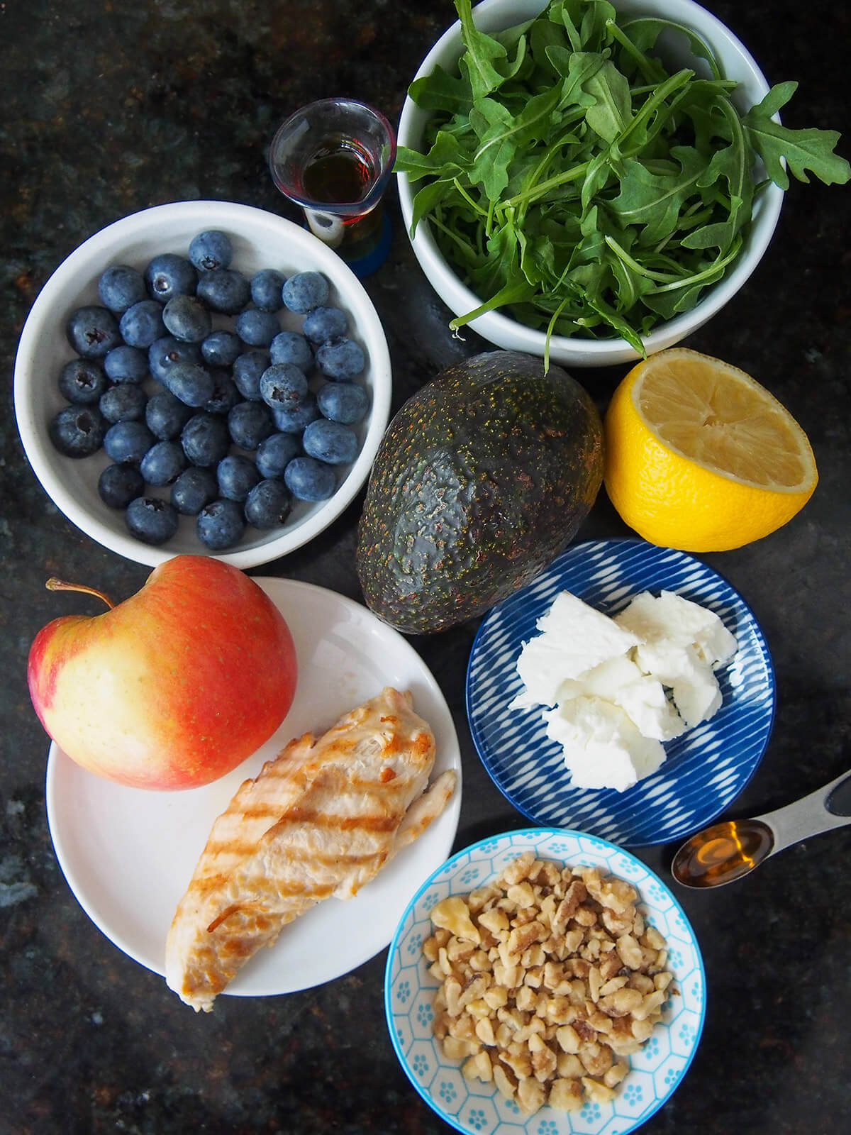 bowls with blueberries chicken, feta, arugula, chicken, apple and nuts with avocado in middle