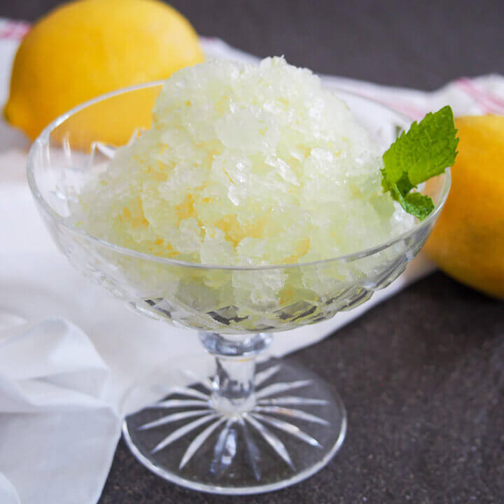 glass of lemon granita with lemons behind