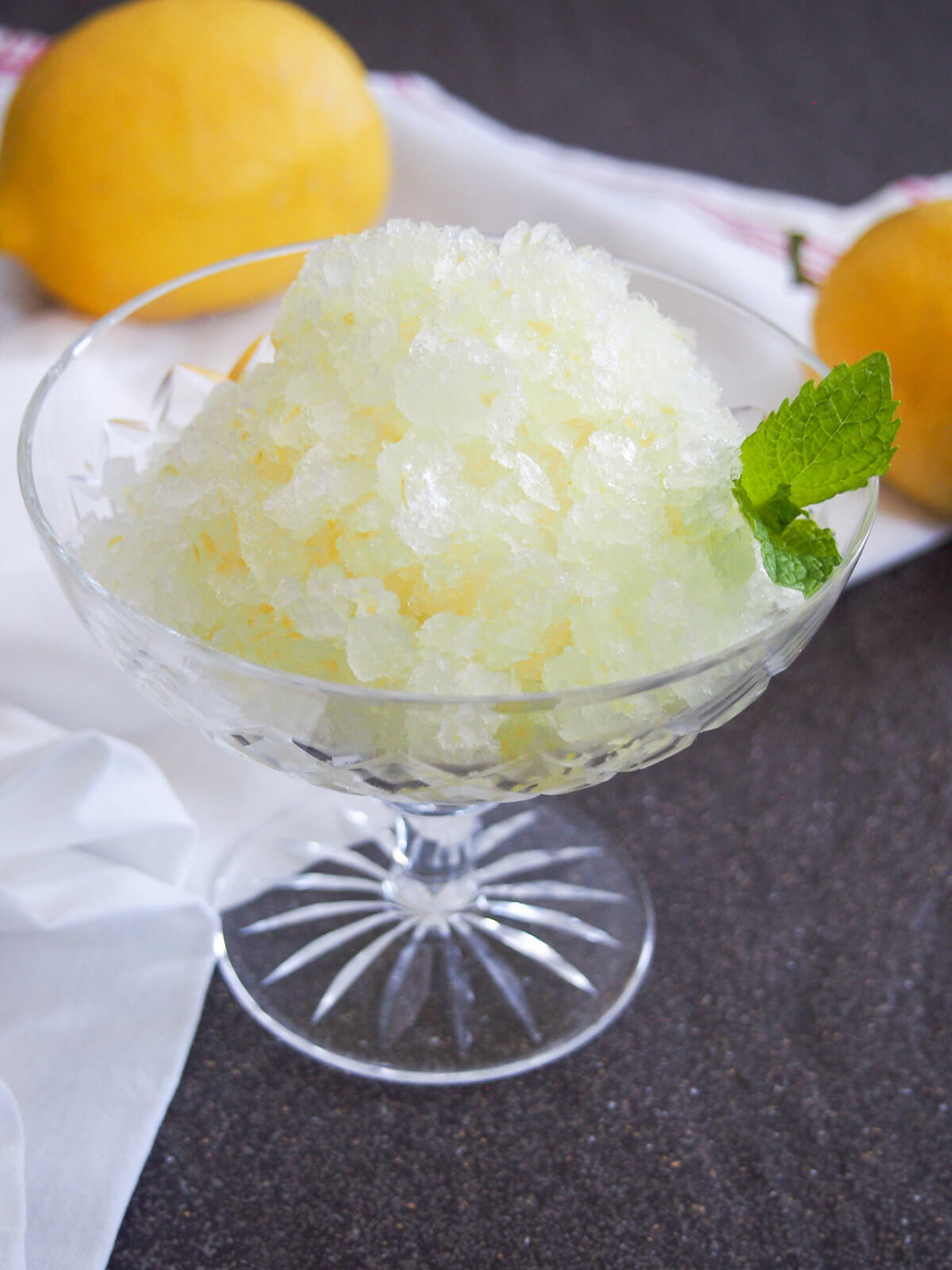 glass of lemon granita with lemons behind glass