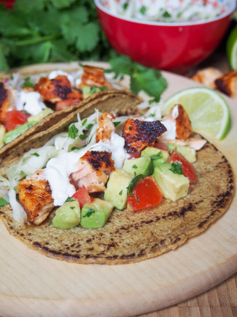 side view of salmon taco with one behind and bowl with slaw in rear