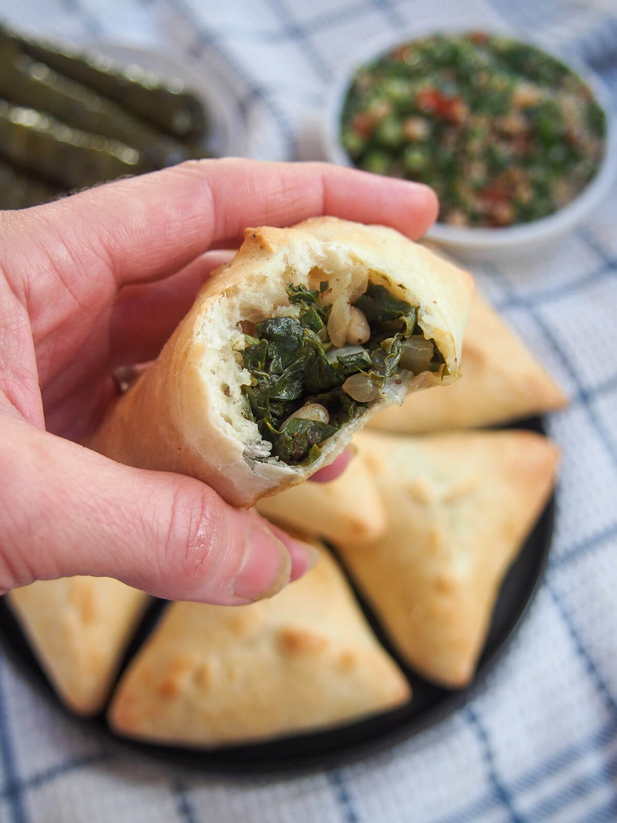 holding a bitten into spinach fatayer in hand over plate with more