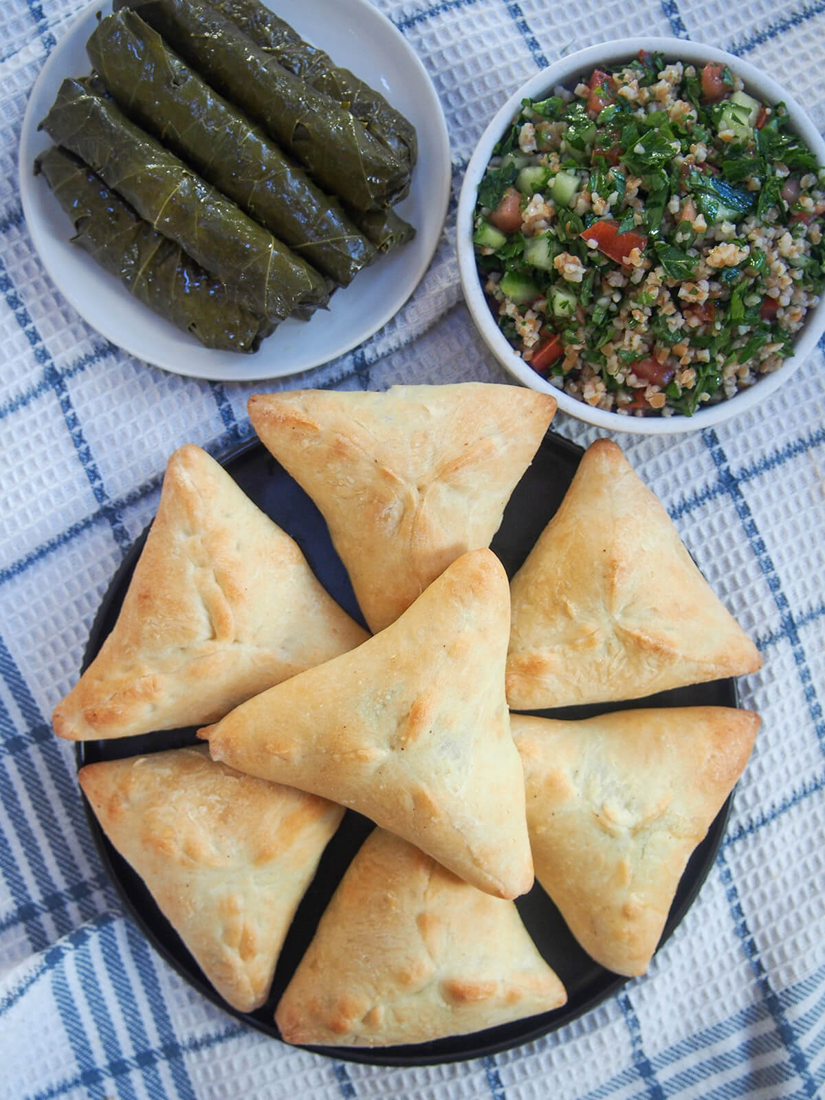 plate of spinach fatayer with plates od salad and grape leaves above from overhead