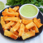 plate of yuca fries with bowl of green sauce for dipping at back right of palte