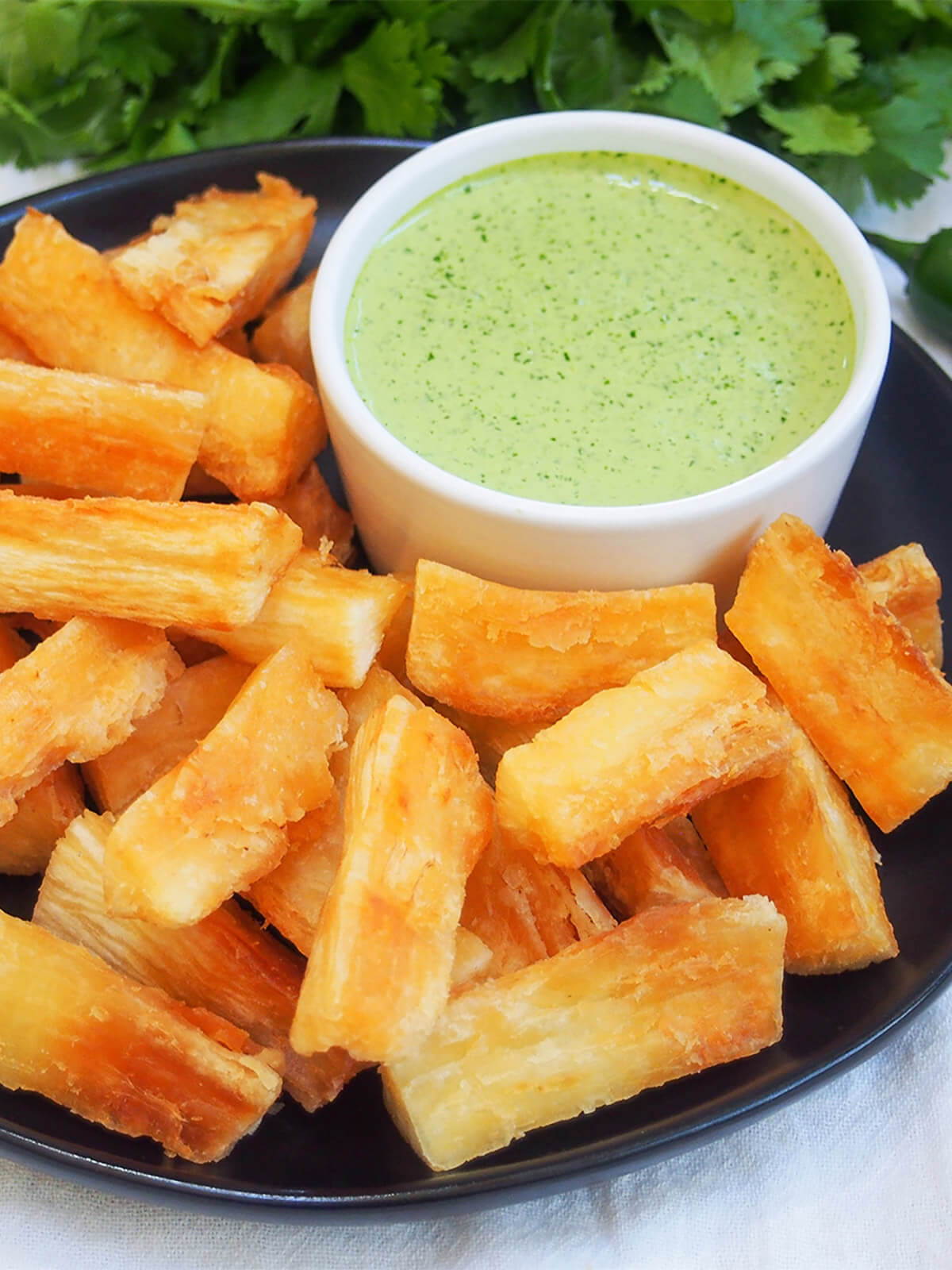 close view of plate of yuca fries with green sauce at back of plate