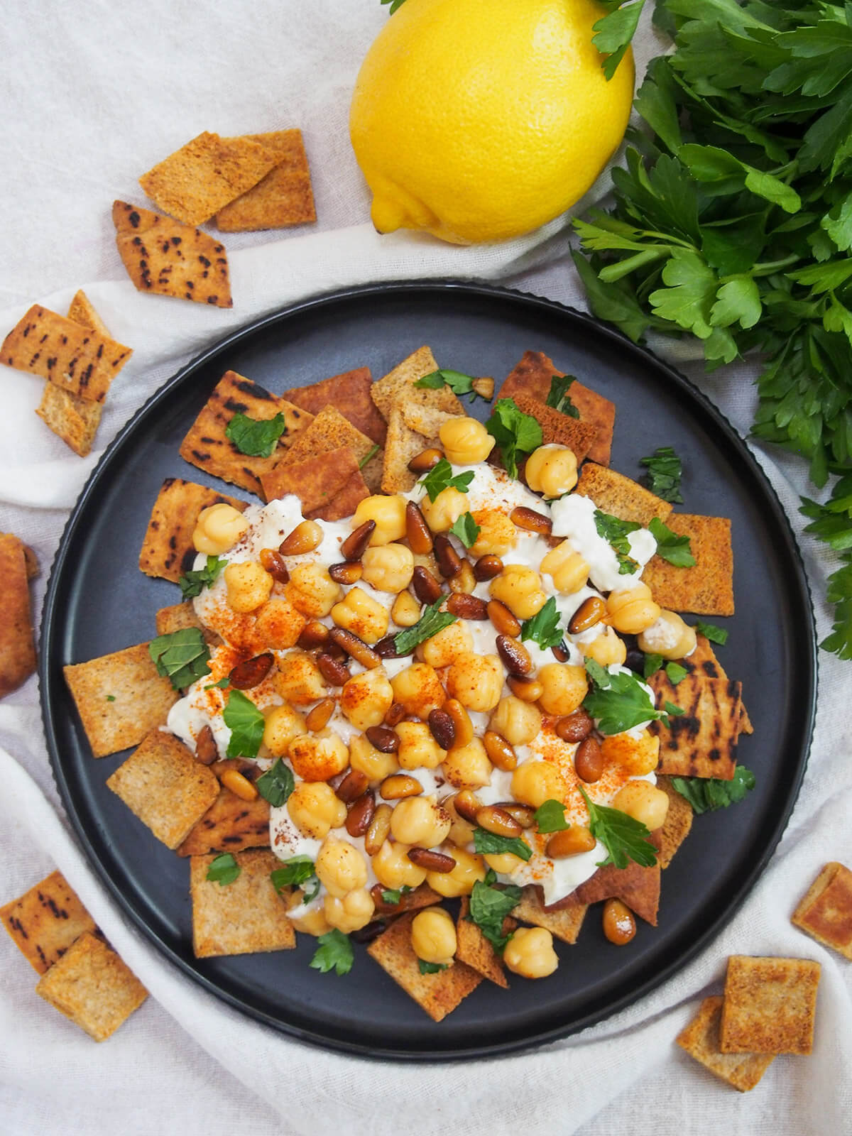 overhead view of plate of chickpea fatteh wih lemon and bunch of parsley above plate