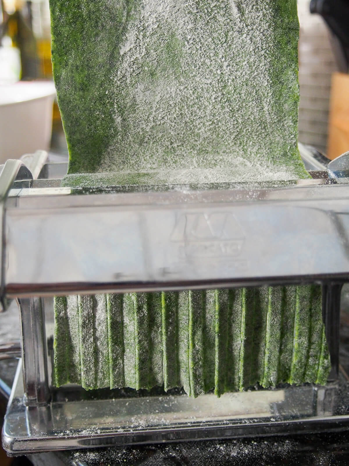 putting a sheet of spinach pasta through machine to cut into fettuccine