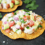 shrimp ceviche tostada with part view of another behind and cilantro on board